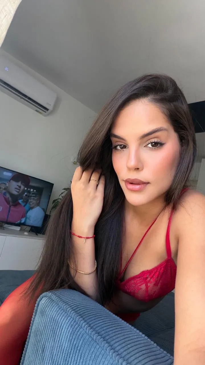 Woman with long dark hair wearing a red lace top.