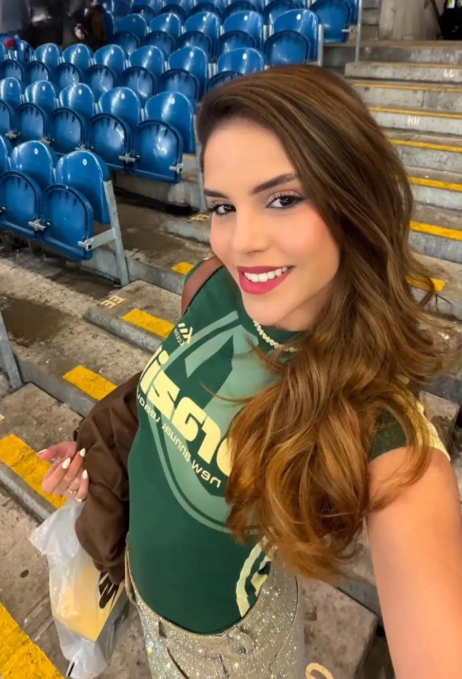 Smiling woman in green shirt at a sports stadium.