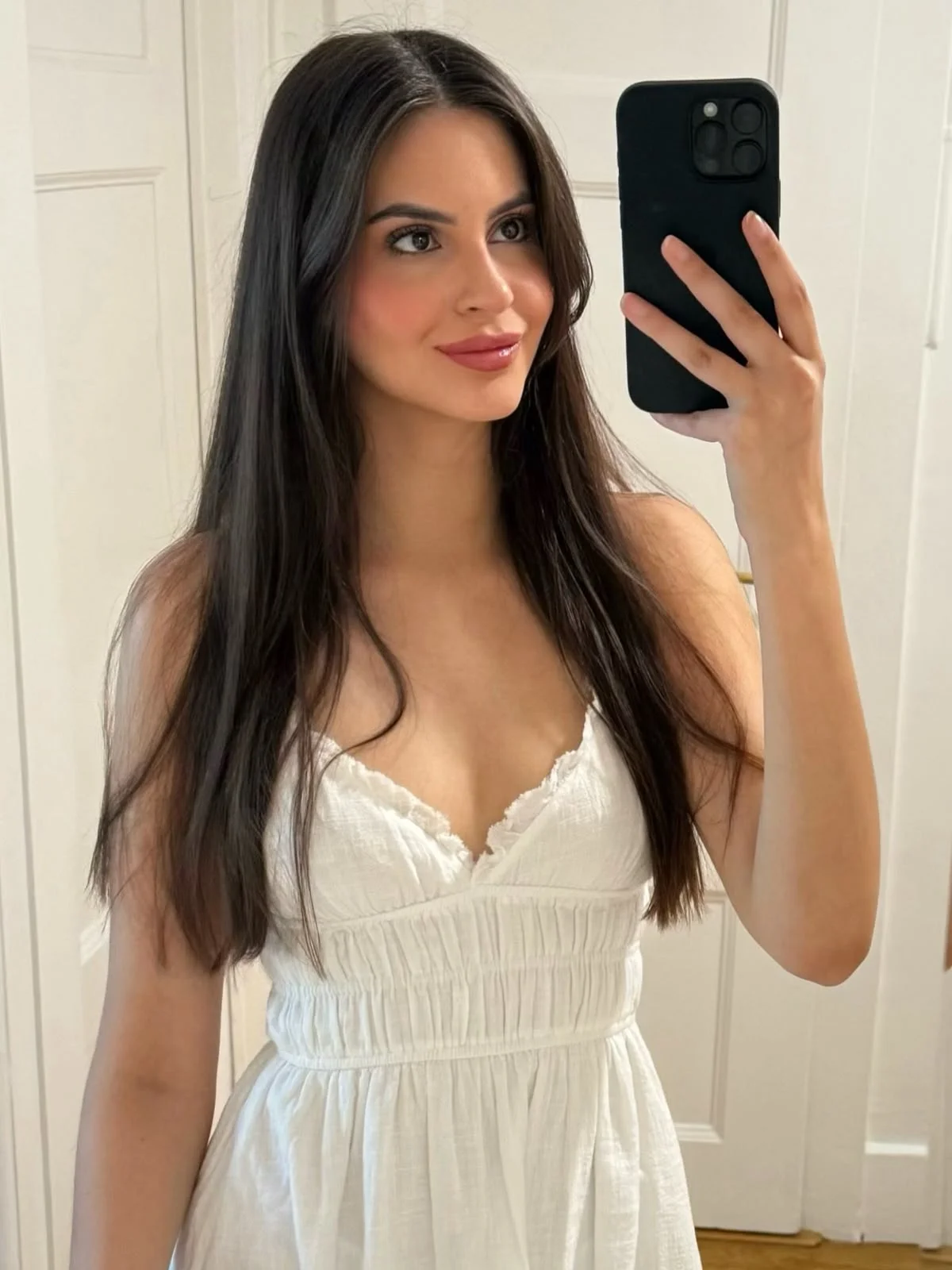 Woman in white smocked dress taking mirror selfie.