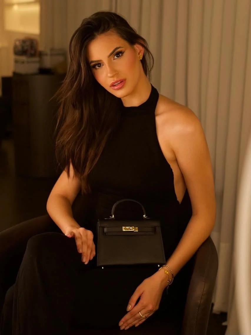Woman in a black halter dress holding a handbag.