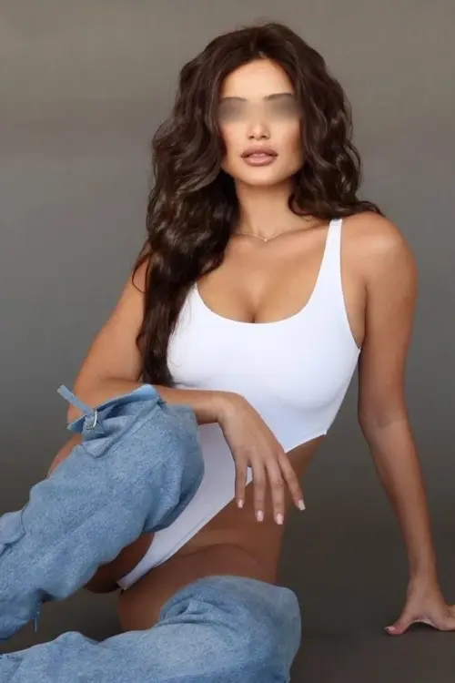 Woman in white bodysuit and over-the-knee denim boots sitting.