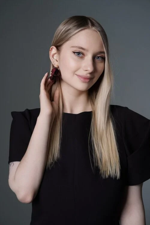 Young blonde woman wearing a black top and flower earring.