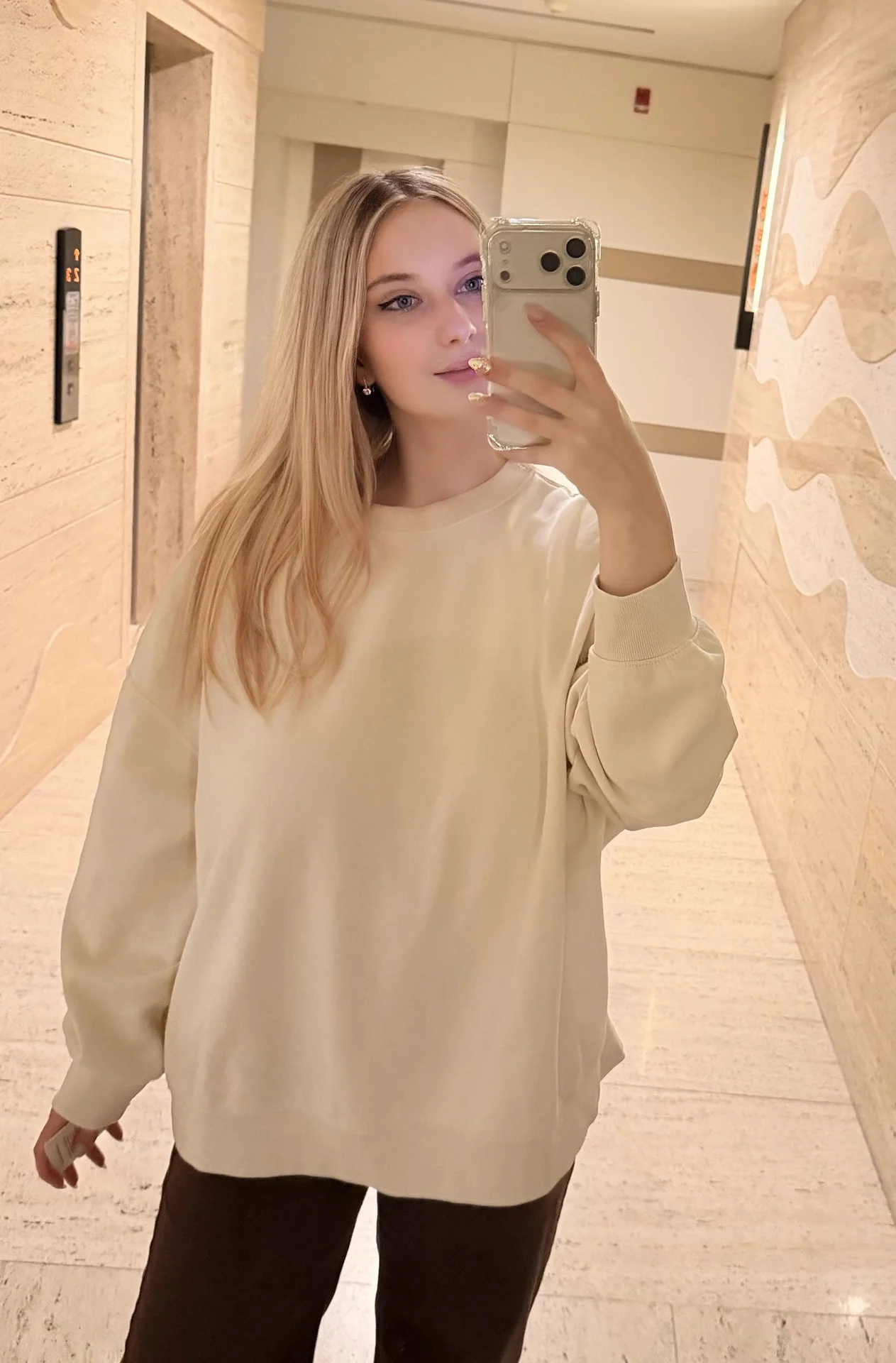 Blonde woman in a cream jumper taking a mirror selfie
