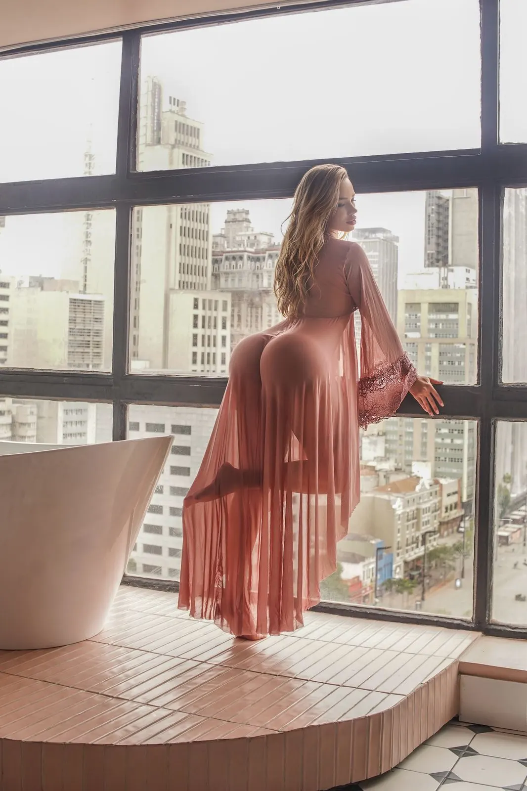 A woman in a sheer pink robe overlooking city skyline.