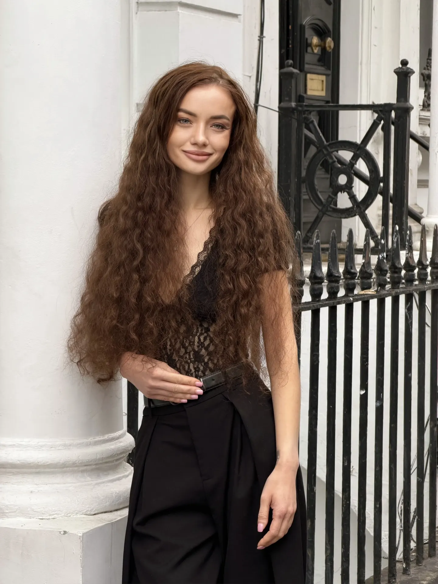 Woman with long curly hair leaning against a white pillar