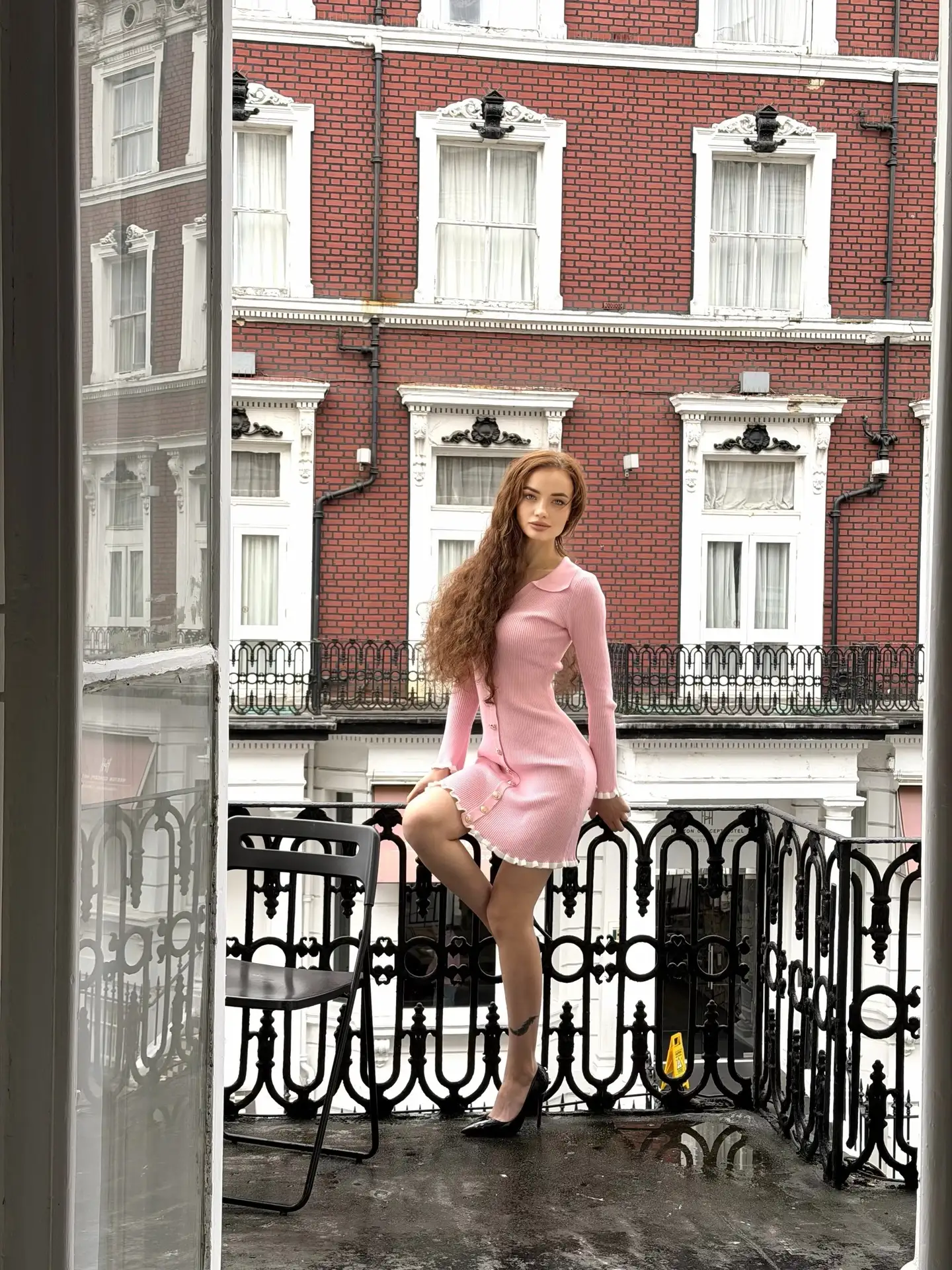 Woman in a pink dress posing on a city balcony.